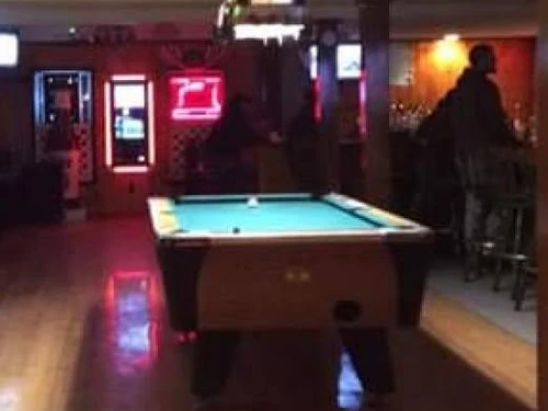 The barroom at Spirits: the pool table under a stained-glass lamp, red neon on the wall, the bar and stools beyond
